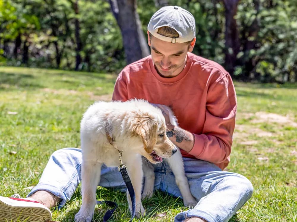 man holding puppy on leash while sitting on the grass